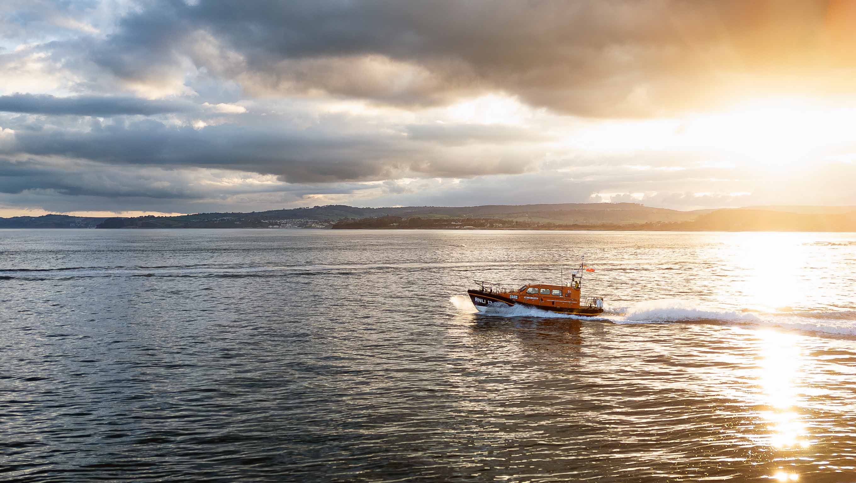 Exmouth's Shannon class lifeboat cruises along calm seas as the sun sets behind the coastline