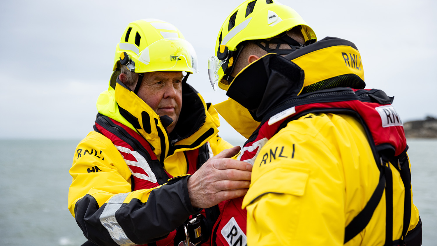 A lifeboat crew member is helping his crewmate with their kit