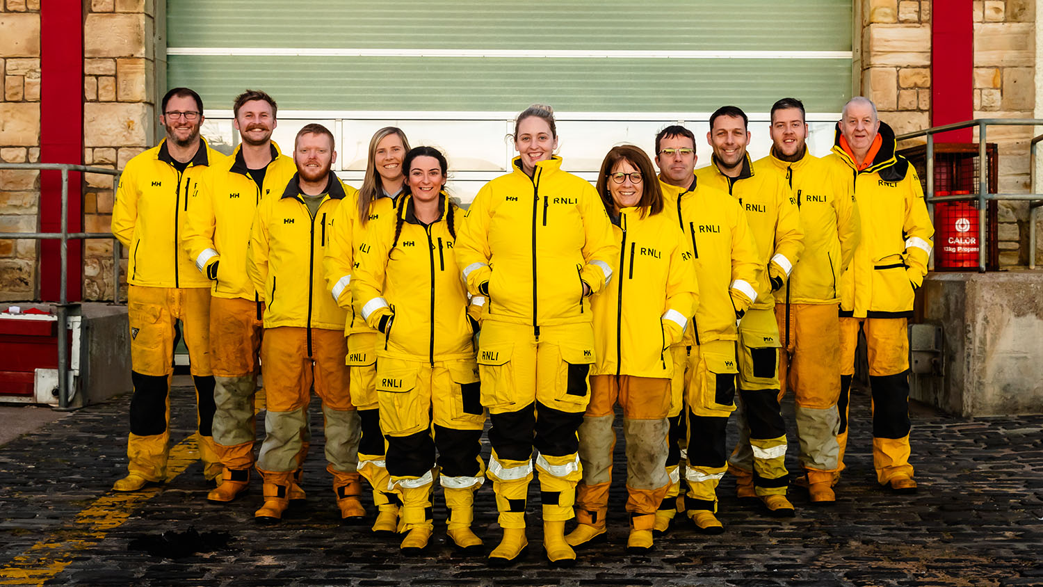 RNLI Anstruther lifeboat volunteers standing in front of the lifeboat station, lined up, facing the camera.