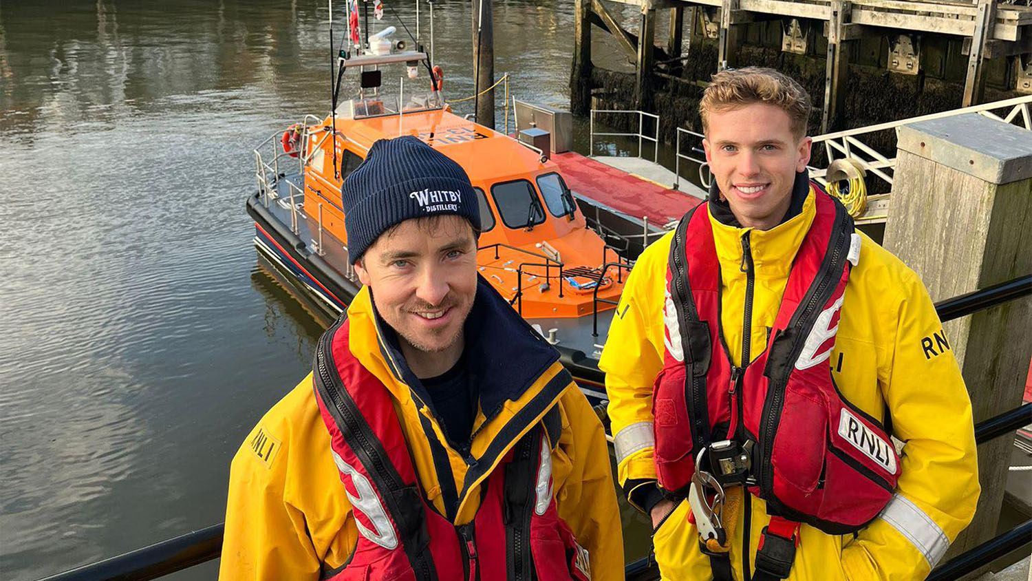 RNLI Whitby crew members Luke Pentith and Max Burnett standing in front of Whitby’s Shannon class lifeboat.