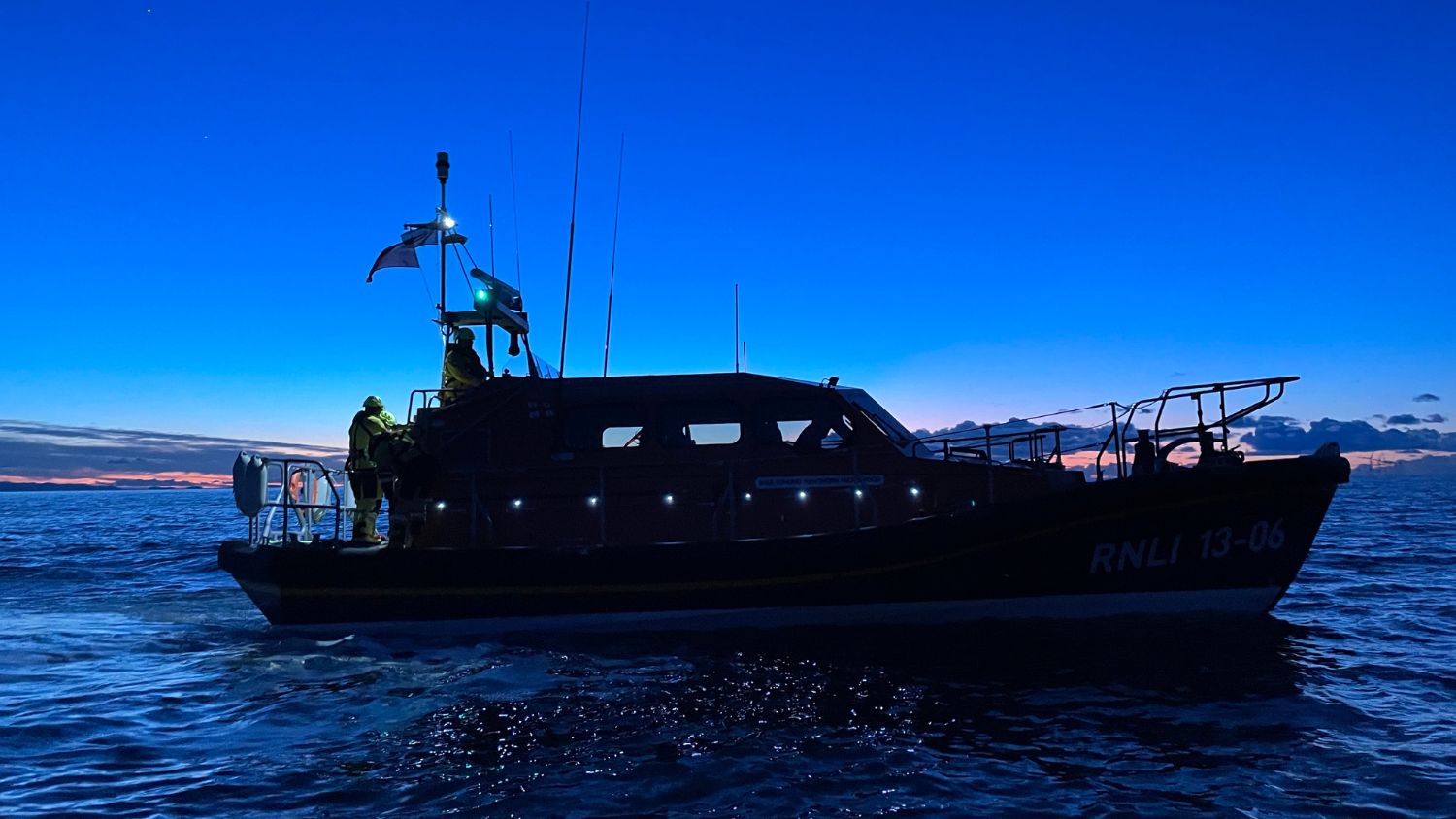 The silhouette of an RNLI Shannon class lifeboat at sea in the fading light.
