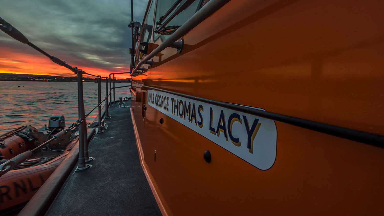Close-up view of the orange hull of a lifeboat named "RNLB George Thomas Lacy" at sunset.
