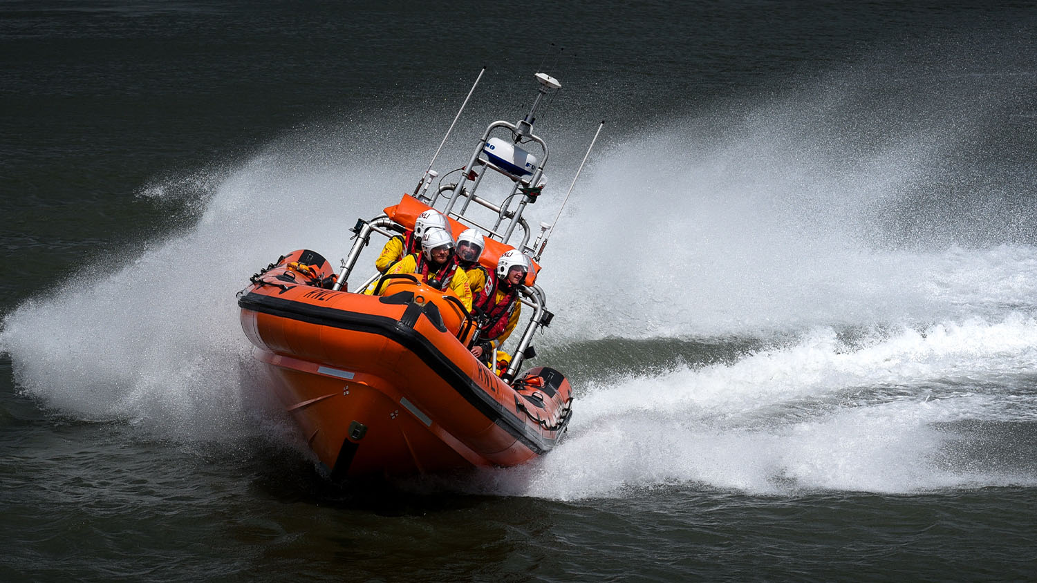 An orange lifeboat speeds across a black, rough sea.