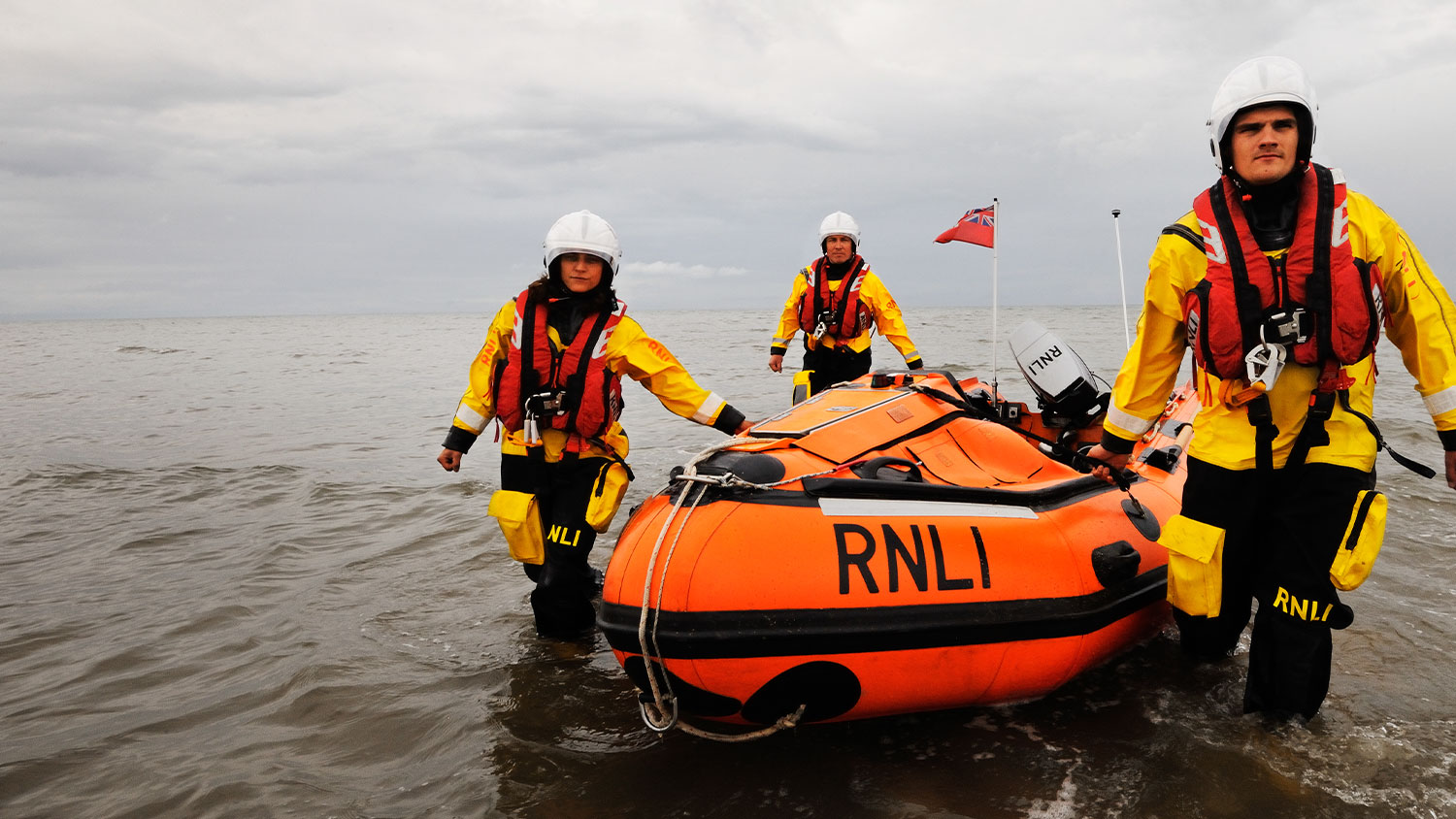 3 lifeboat crew in kit walking in water, pulling an inshore lifeboat