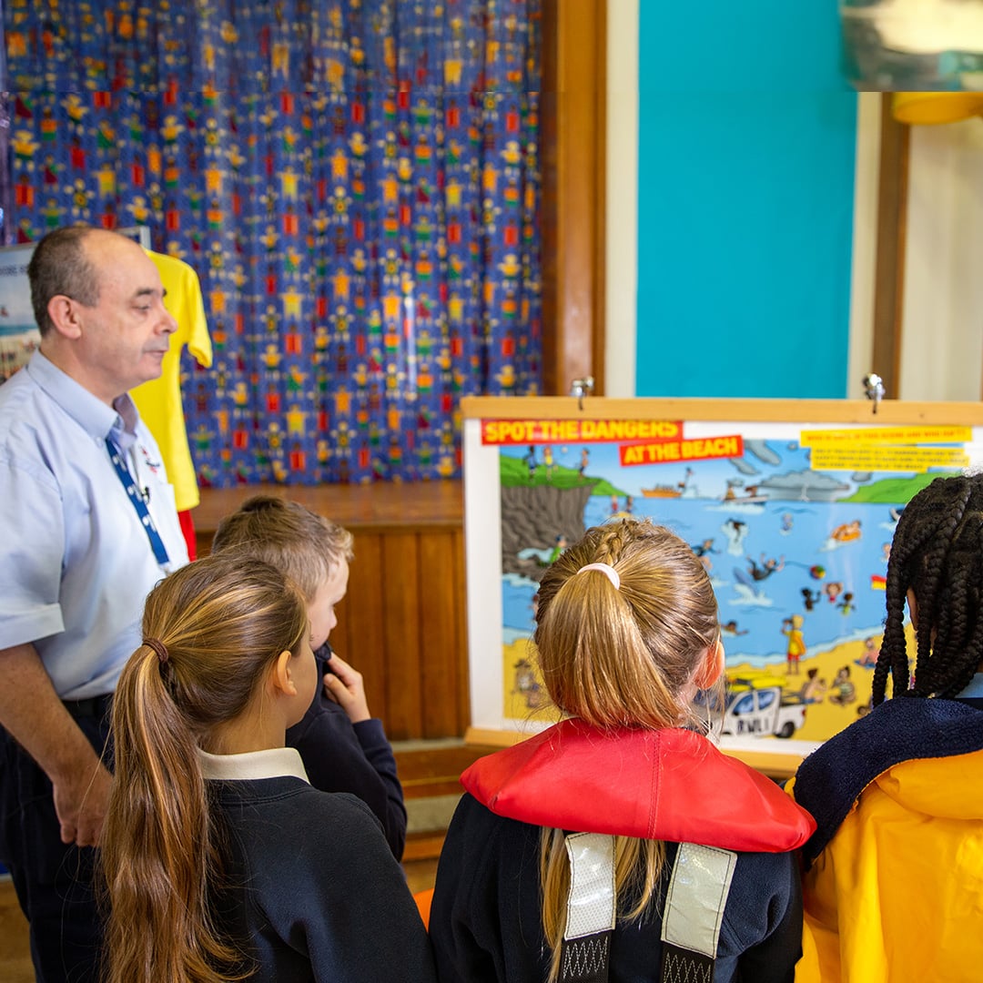 Group of children and a water safety volunteer circled around a flip chart, learning about the dangers at the beach.