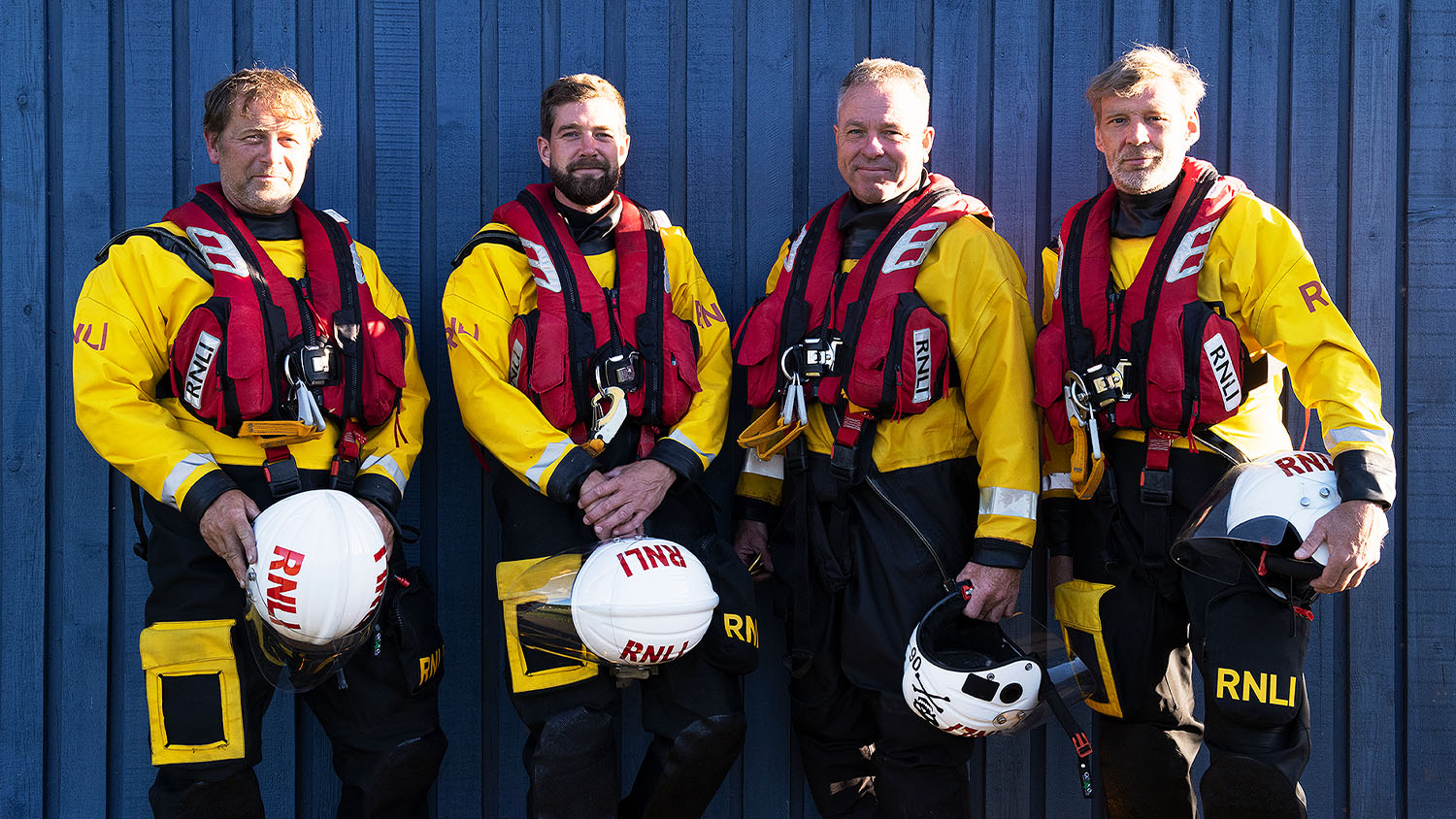 Four Dart lifeboat volunteers stood outside of the boathouse all wearing full crew kit