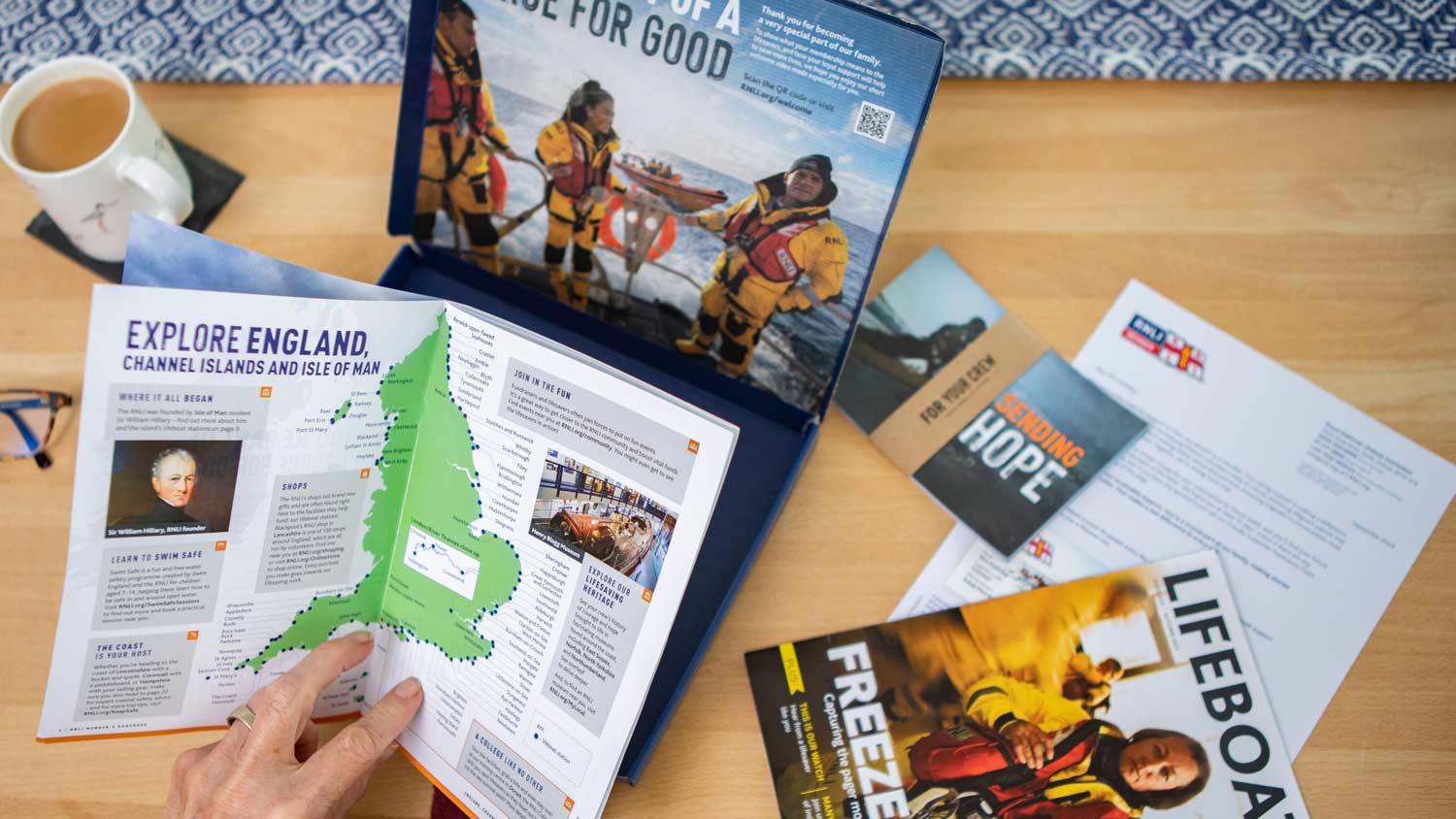 A woman reads through the contents of the RNLI membership pack. Including the welcome guide, Lifeboat magazine, postcards, welcome letter and the gift box.