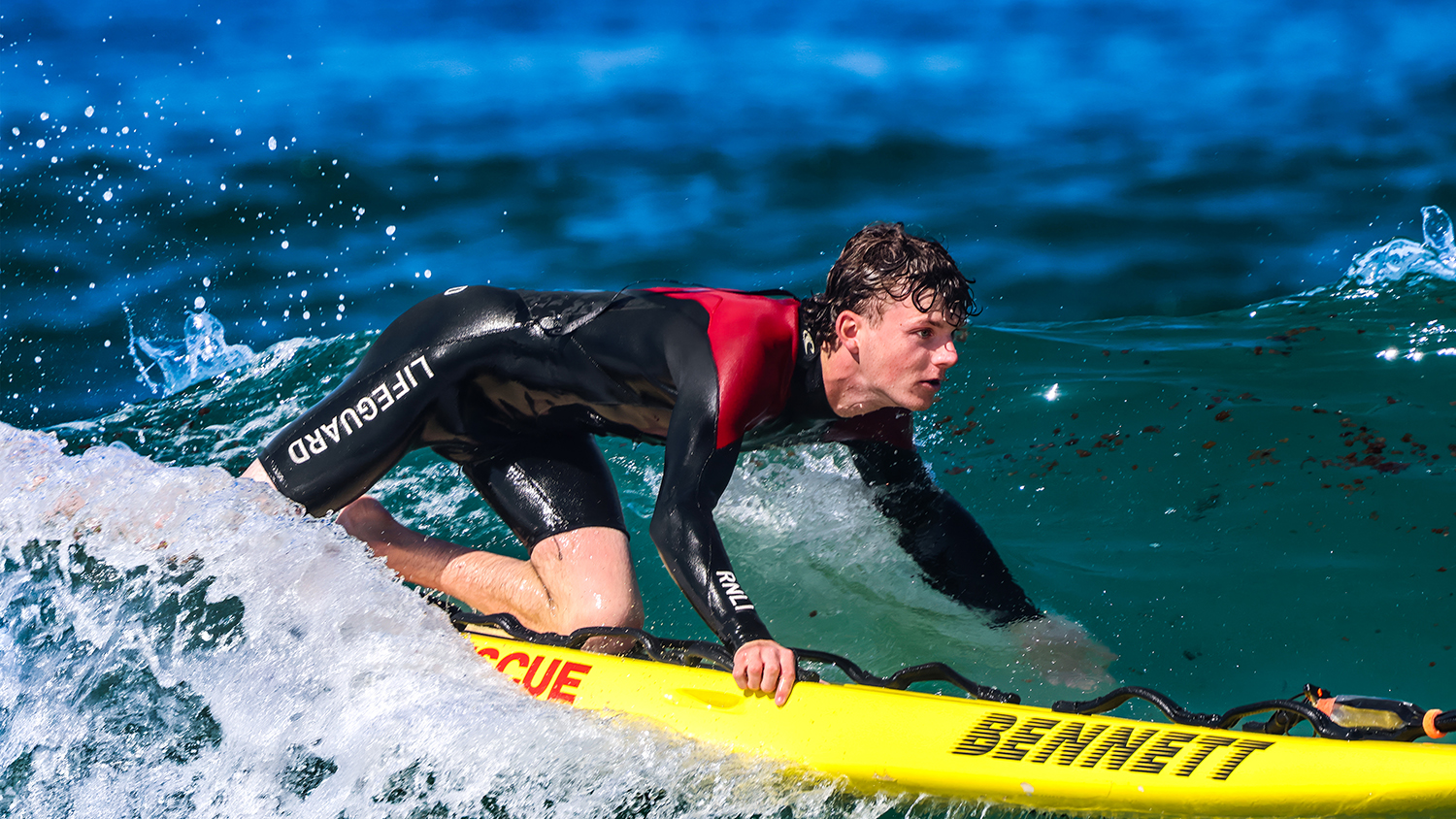 A lifeguard on a yellow rescue board paddles through the waves.
