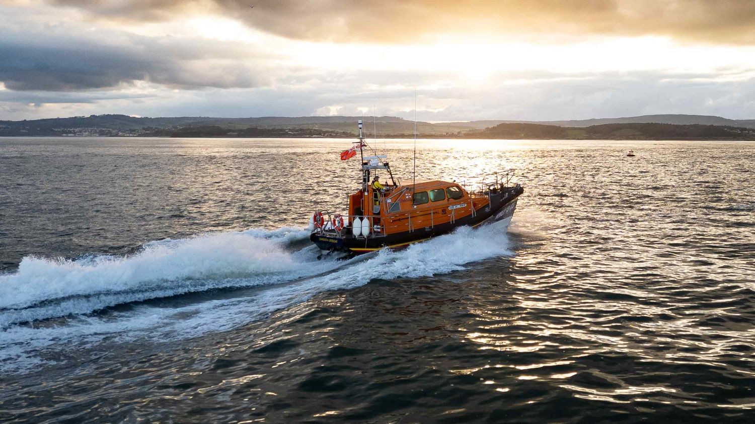 Exmouth's Shannon class lifeboat cruises along the sea at sunset on calm seas and partly clouded skies