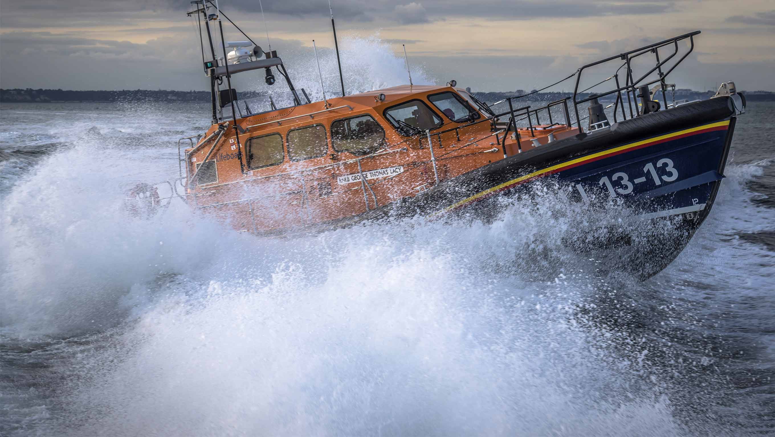 Swanage RNLI’s Shannon class lifeboat 13-13 powering through choppy water, surrounded by lots of white spray and dark clouds above 