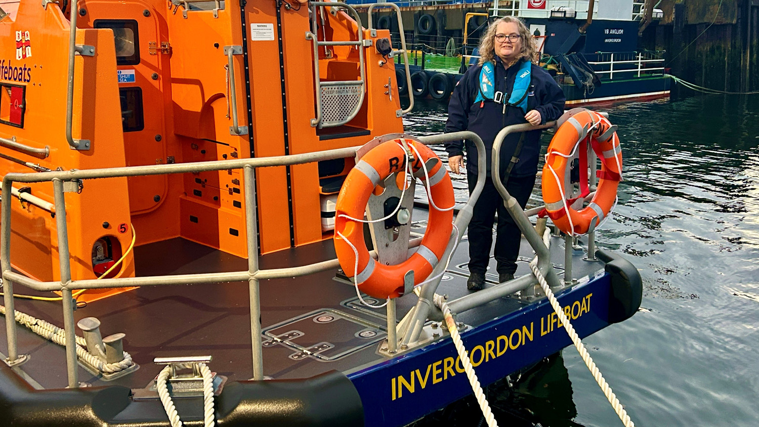 Invergordon Launch Authority Jacqueline Macfarlane standing at the stern of the station’s Shannon class all-weather lifeboat. The lifeboat is moored and Jac is wearing a blue RNLI lifejacket.