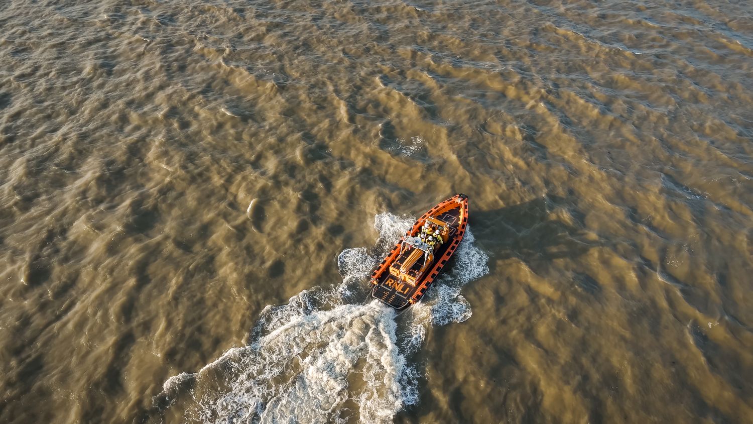 An aerial photo of an E class lifeboat and its crew on the River Thames. It is leaving a wake of white water behind it. 