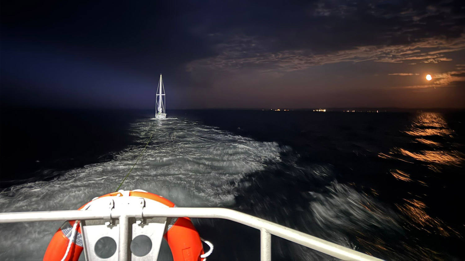 View from the rear deck of Anstruther’s Launch a Memory Shannon class lifeboat as it tows a yacht at night-time