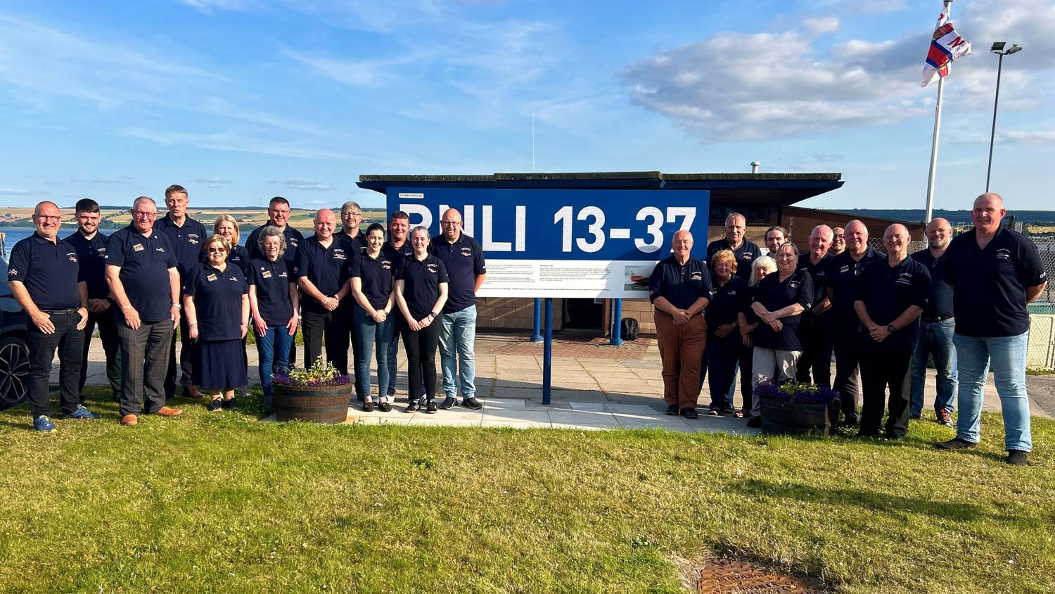 The crew of Invergordon lifeboat station pose on the grass next to the Launch A Memory poster featuring names of all the loved ones on their lifeboat 