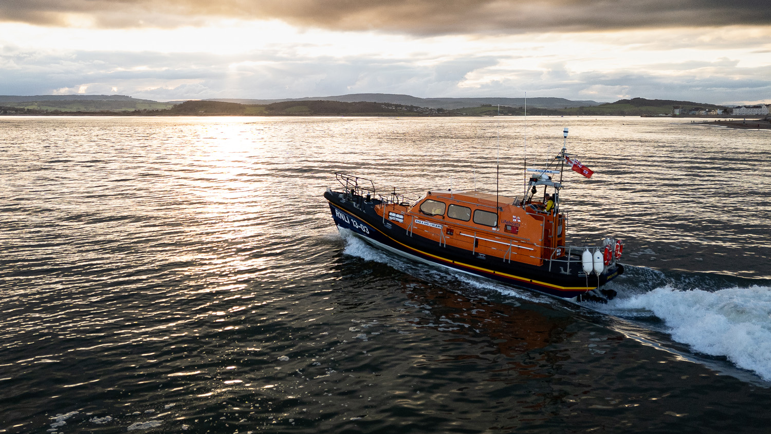 A large orange boat motors across a calm sea