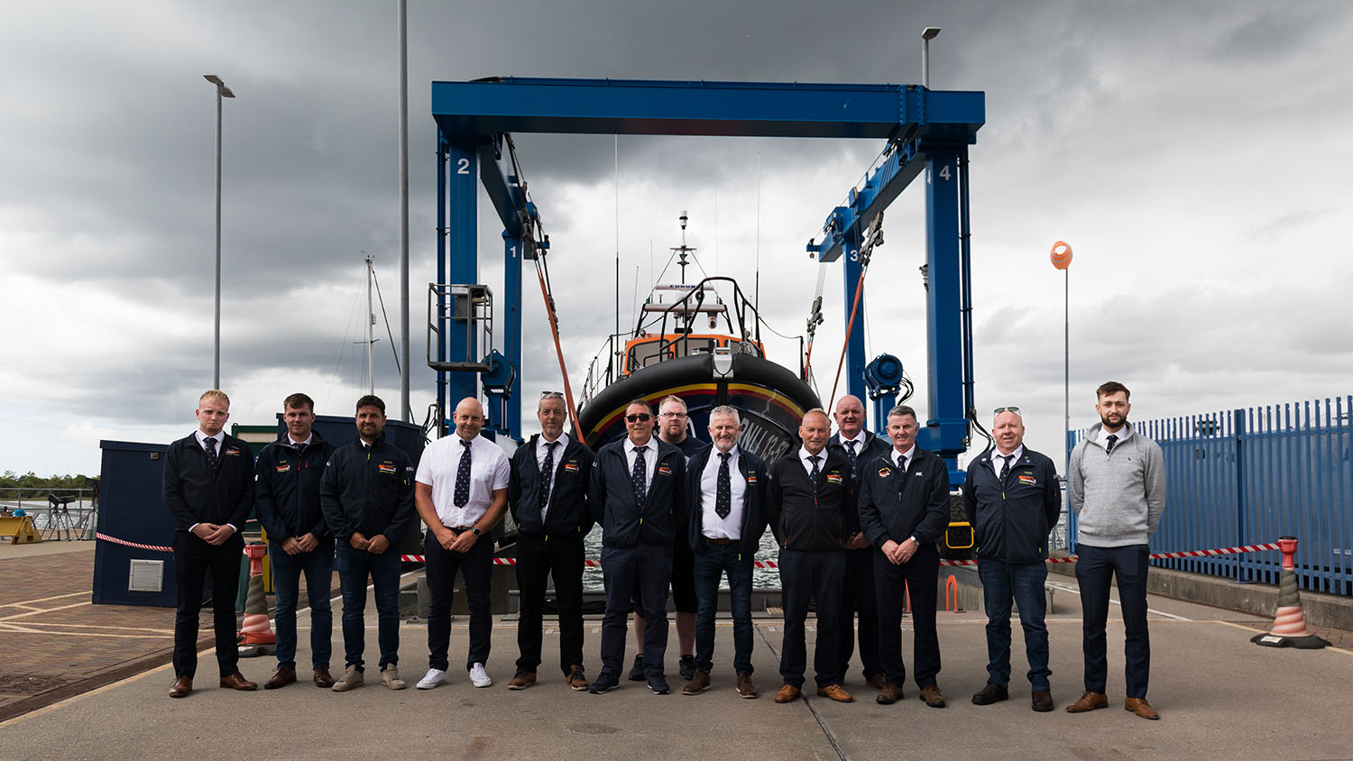 The Kilkeel crew are standing in a line in front of their new Shannon class lifeboat Bobby Cameron 13-57. They are at the All-weather Lifeboat Centre in Poole, Dorset, for the lifeboat’s bell ringing ceremony.