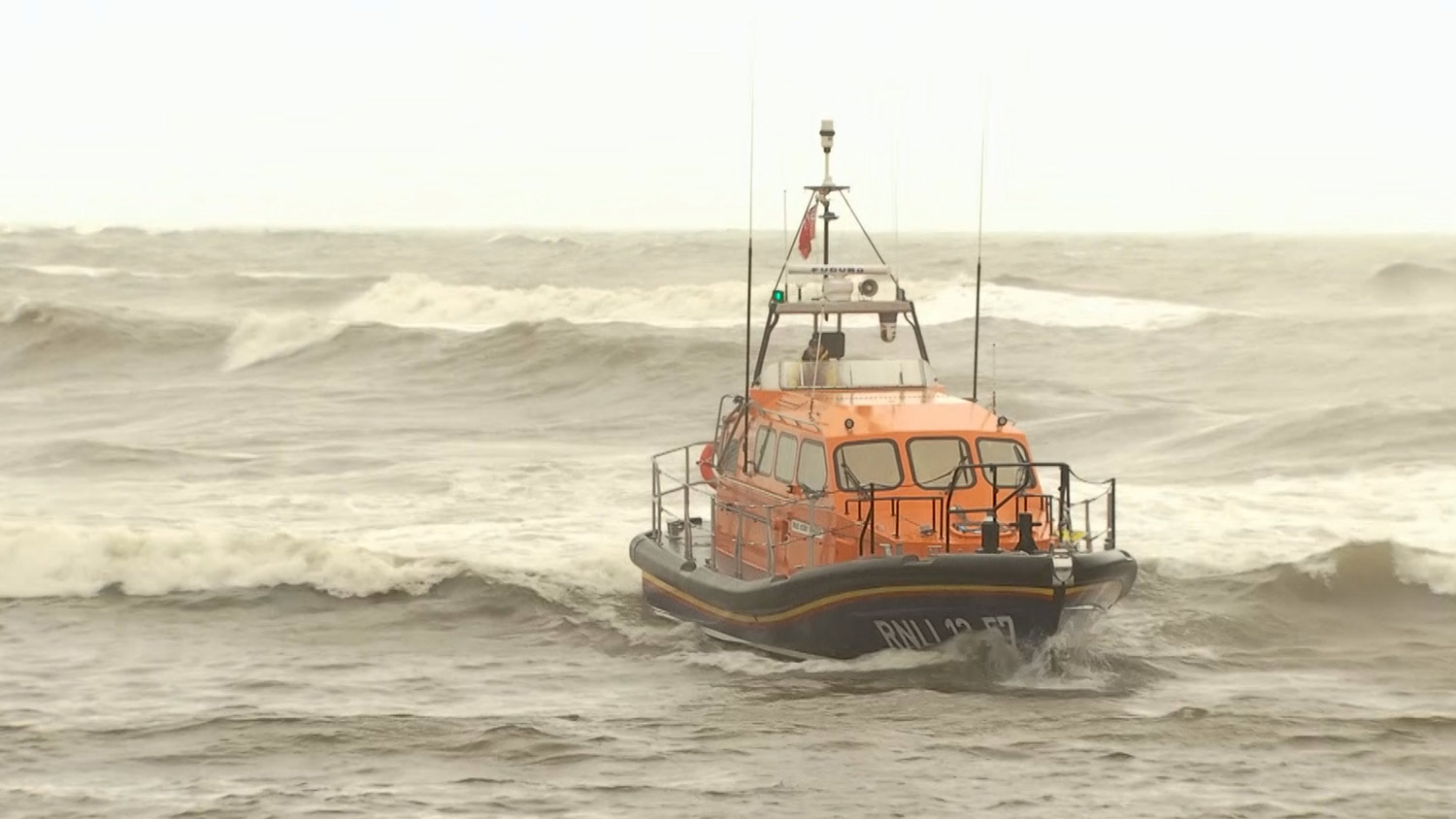 Kilkeel Shannon class all-weather lifeboat motors over breaking waves under clouded skies