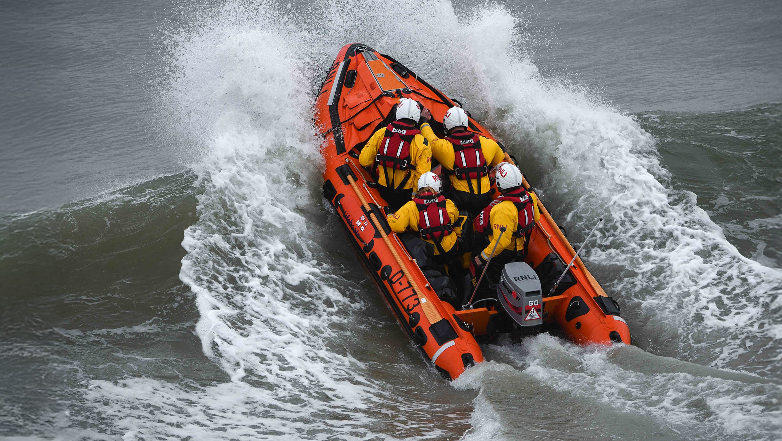 D class lifeboat with four crew members aboard launches dramatically through the waves.