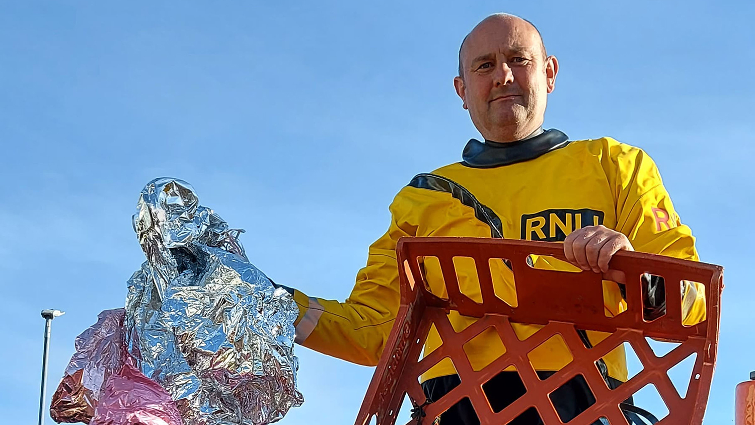 Burnham RNLI Helm Stuart looks into the camera, holding up a deflated helium balloon and a plastic basket