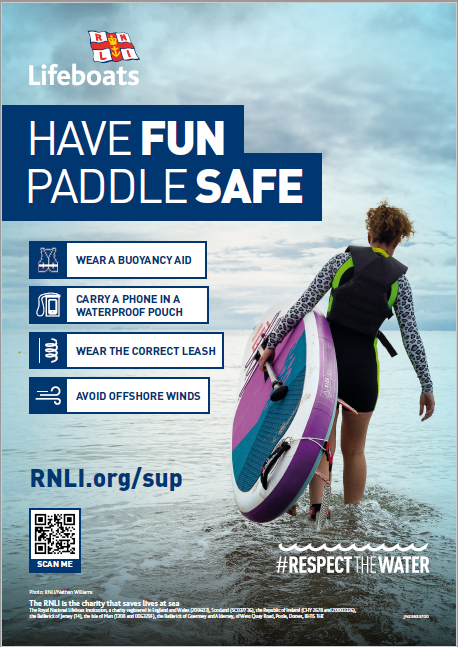person wearing wetsuit holding stand up paddle board under arm 