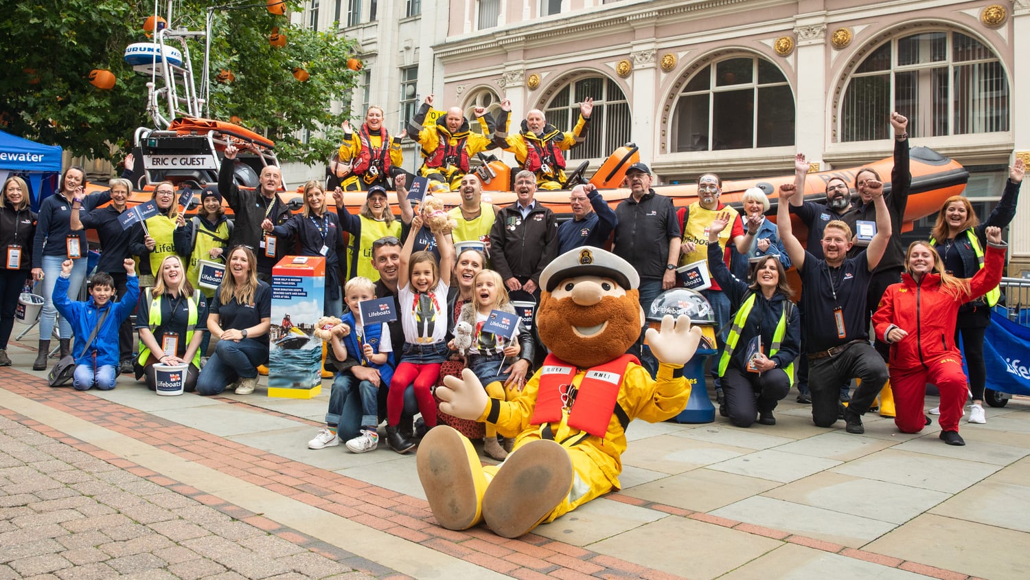 A photo of a group of RNLI crew, lifeguards, fundraisers, and supporters celebrating with Stormy Stan in front of an Atlantic lifeboat
