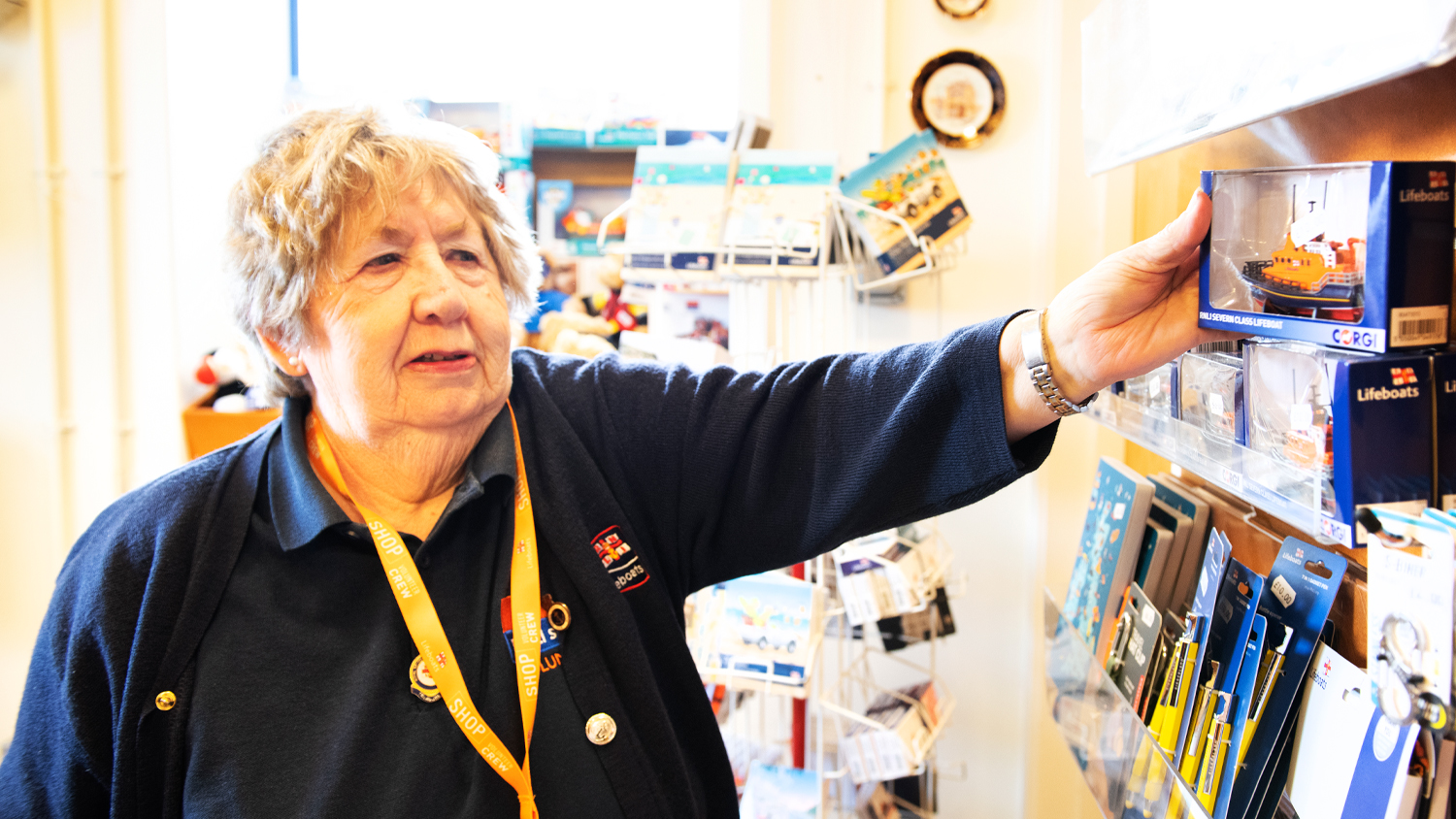 An RNLI shop volunteer stood next to a product display stand.