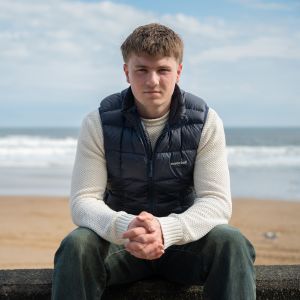 Euan Gray sitting on a wall in front of a beach