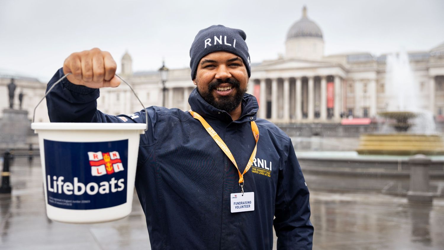 A smiling RNLI fundraising volunteer holding a collection bucket.