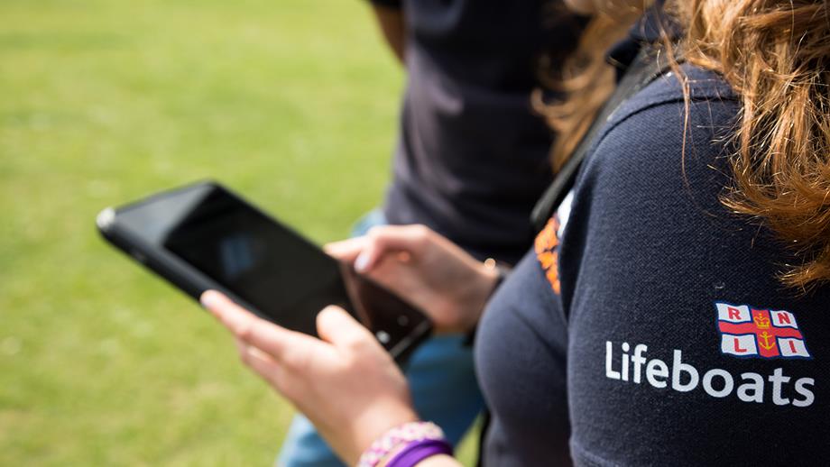 A close-up of an RNLI volunteer using a smartphone.