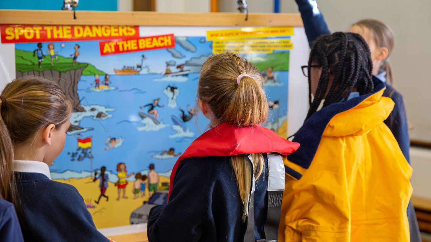 A group of schoolchildren looking at an activity poster about spotting dangers at the beach.