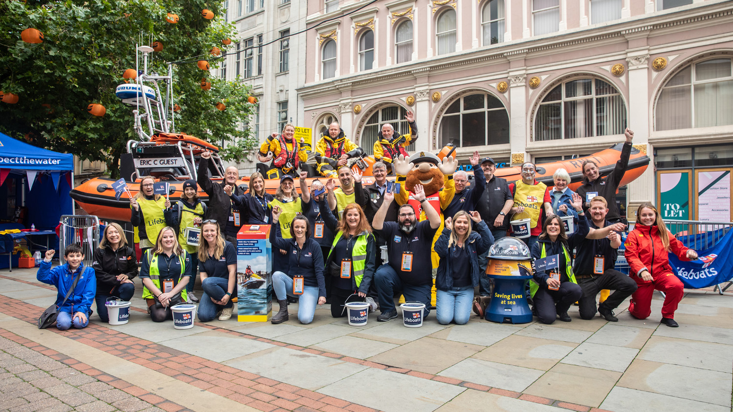 The RNLI family – fundraisers, supporters, crew and other volunteers – line up with a B class lifeboat, recreating the first fundraising street collection, that took place in Manchester in 1891