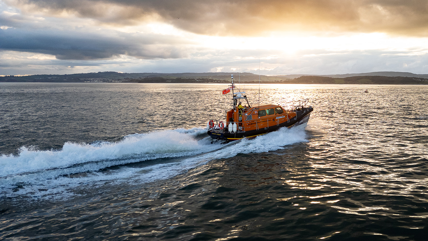 A lifeboat powering out to sea at sunset.