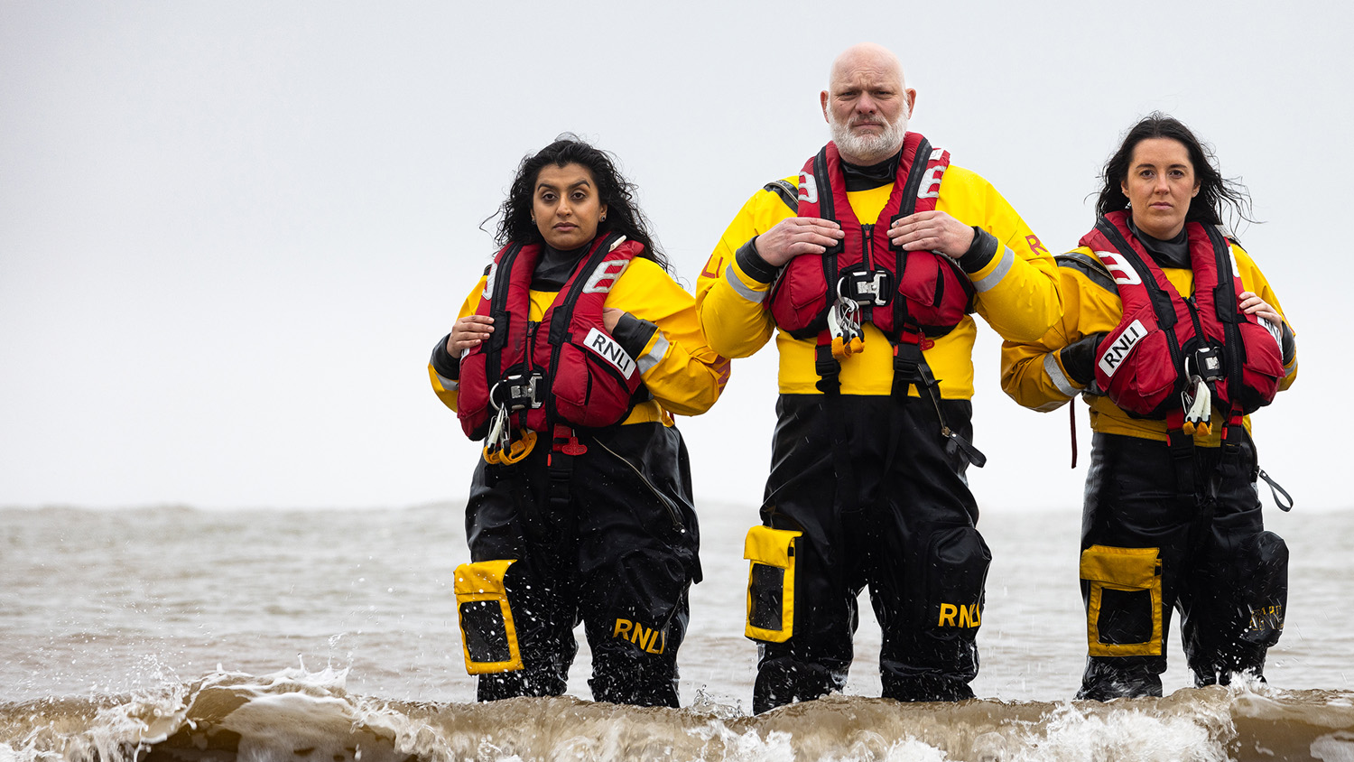Group shot of RNLI volunteer crew in ILB kit standing in the sea, shot in Lyme Regis