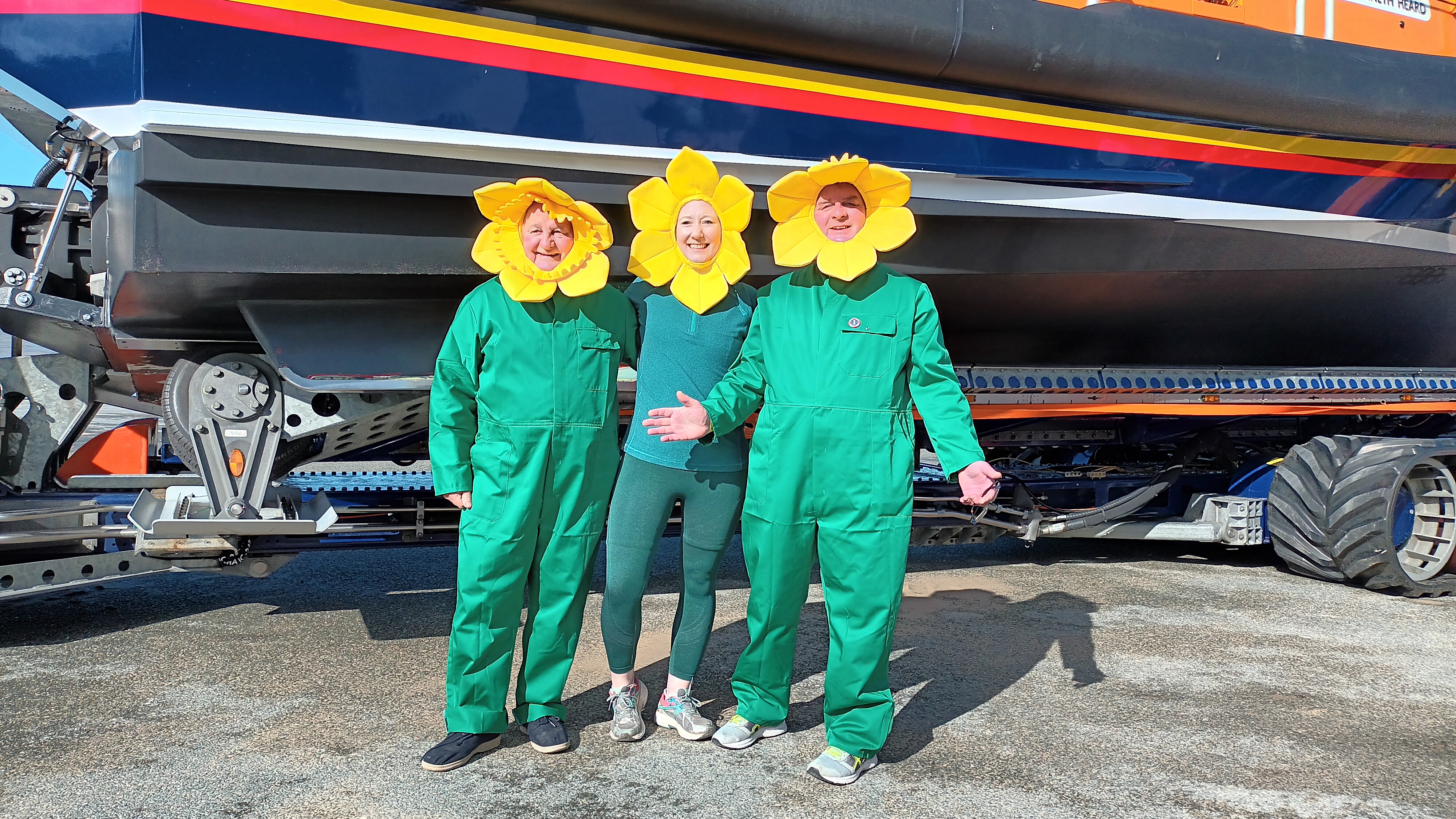 Three people dressed as daffodils stood in front of an All Weather Lifeboat on a trailer.