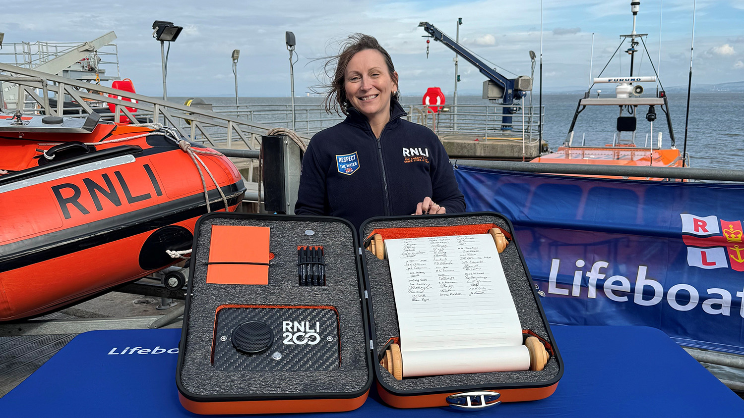 Alison Byers standing behind a commemorative scroll that travelled around RNLI communities as part of the 200th anniversary.