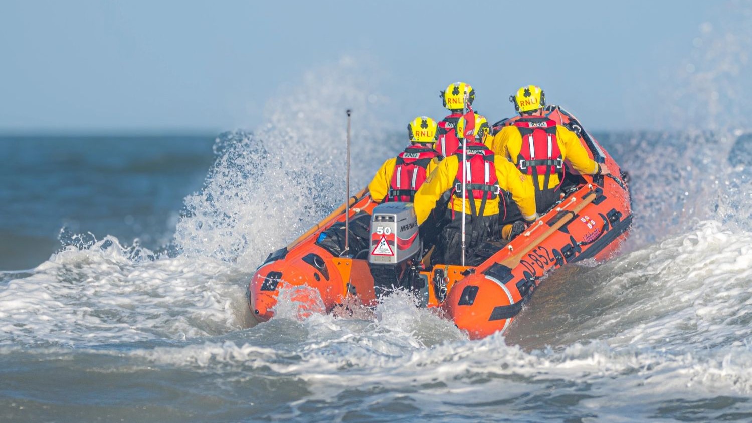 An inshore lifeboat with four crew member on board travelling away from the camera.