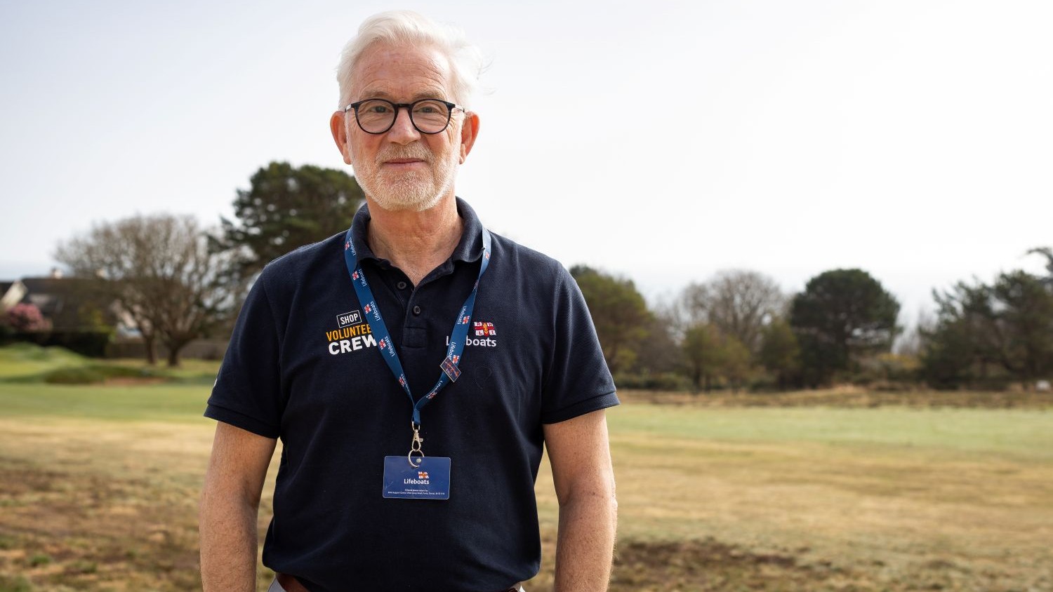 A man with short grey hair and black framed glasses. He is wearing a navy RNLI polo shirt.