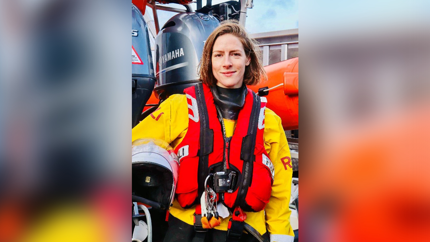 Lucy Maling smiling, while wearing RNLI crew kit and holding a helmet.