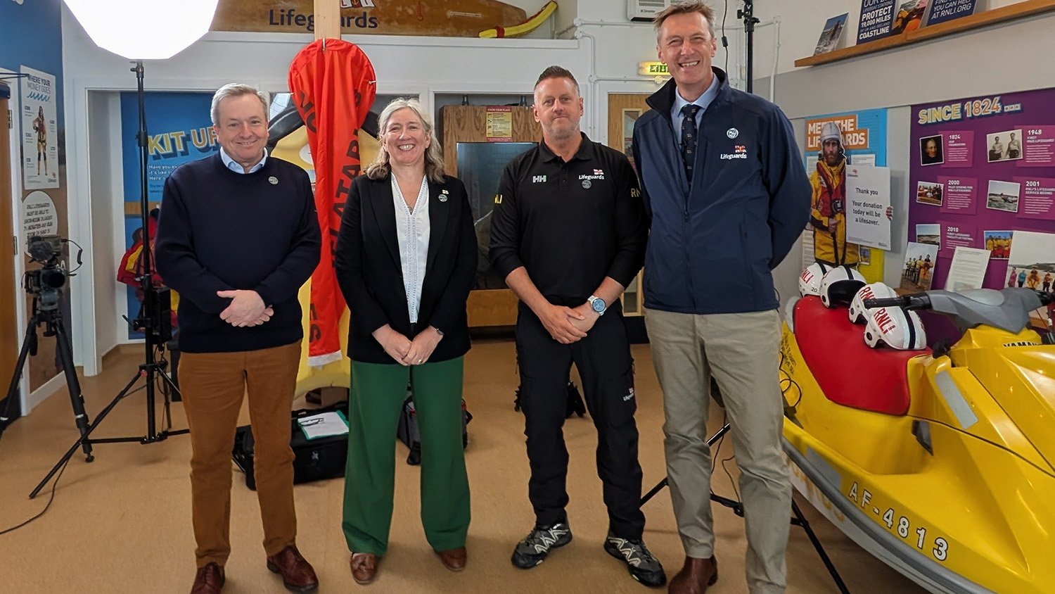Four people standing and smiling inside a Lifeguard Visitor Centre.