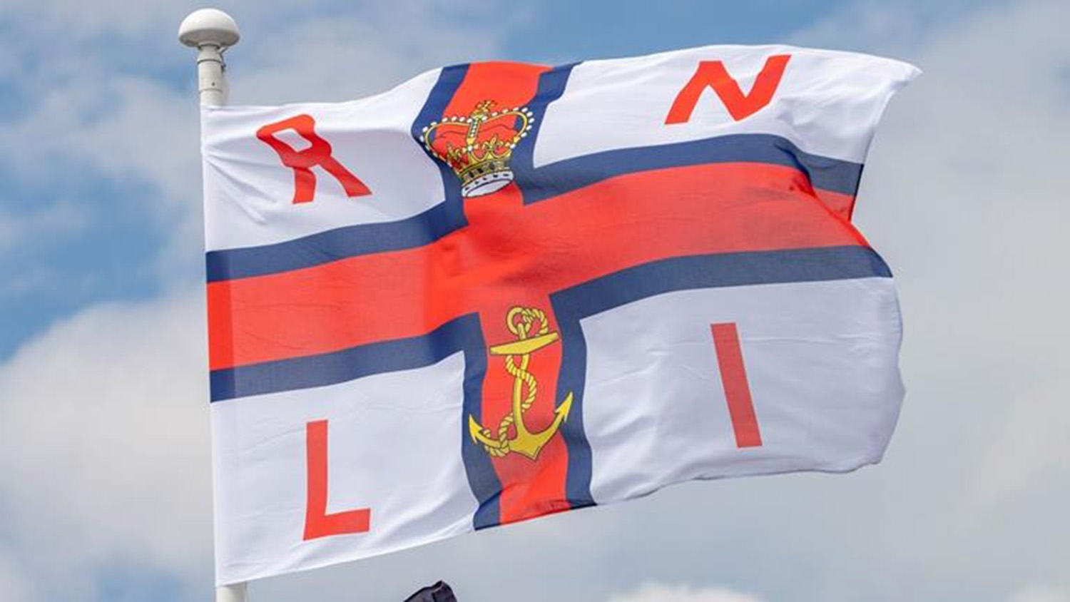 RNLI flag blowing in the wind against a blue sky.