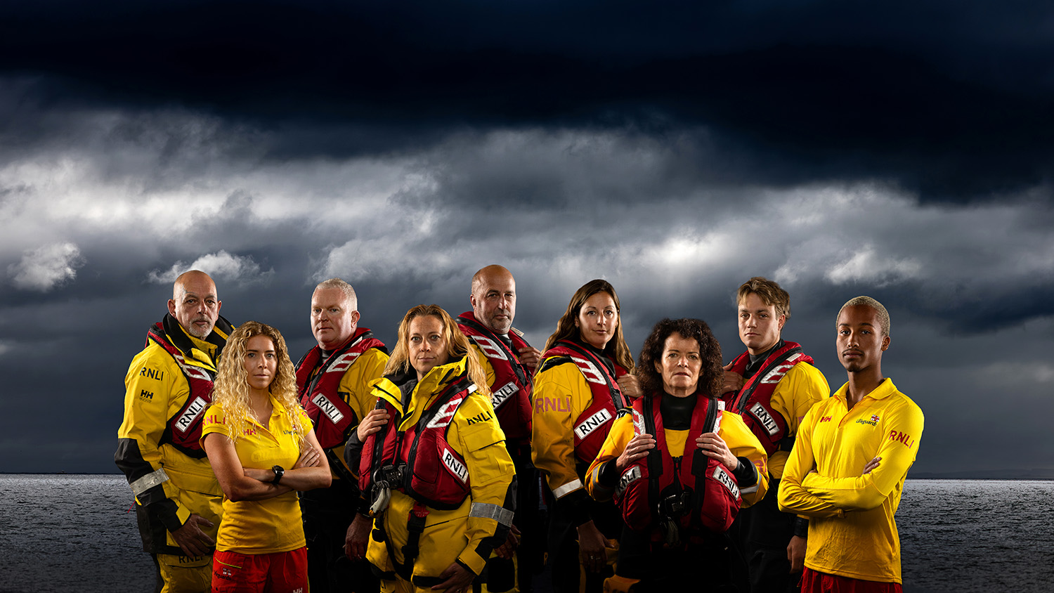Group of RNLI crew members and lifeguards posing in front of a moody sky.