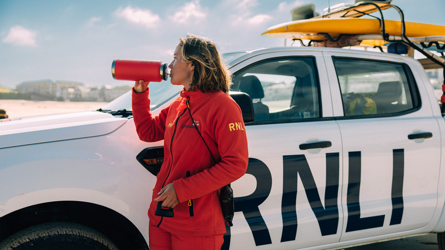 RNLI lifeguard on the beach drinking from a red bottle.