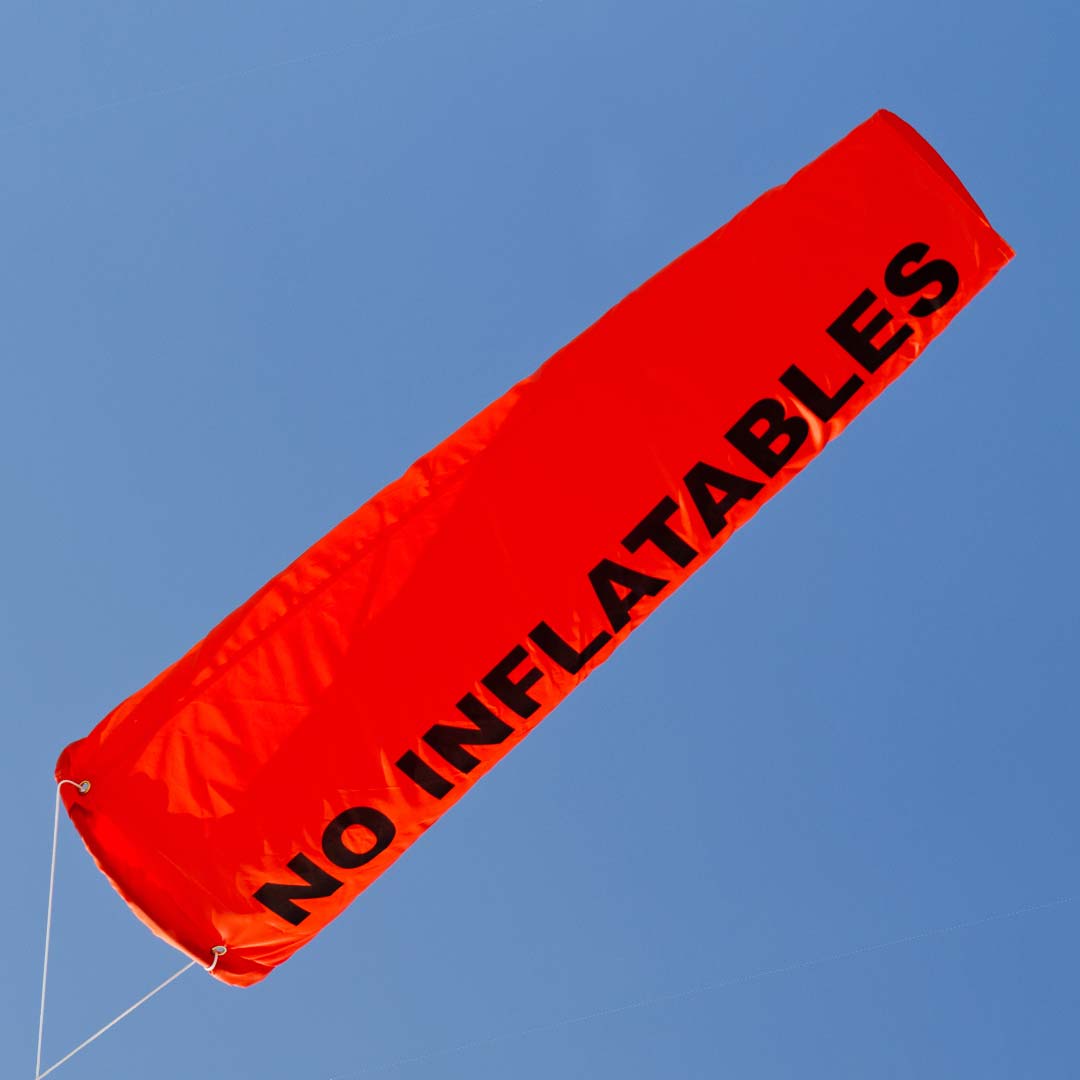 Bright orange windsock blows in the wind with no inflatables written on the fabric