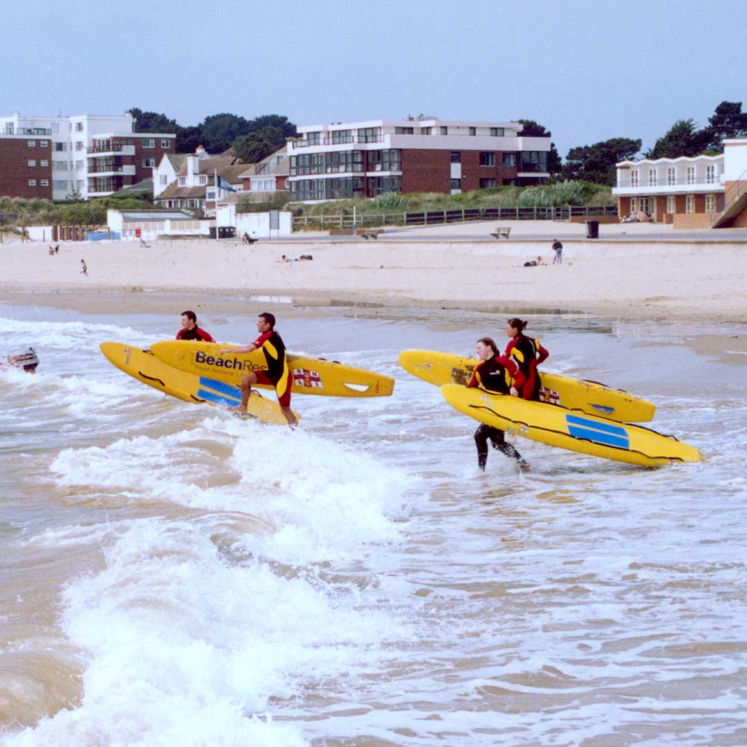 A team of RNLI lifeguards run into the surf carrying bright yellow rescue boards as part of a training exercise. 