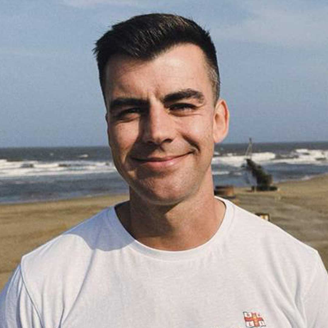 RNLI Lifeguard Supervisor Arun Gray stands on the veach wearing a grey t-shirt