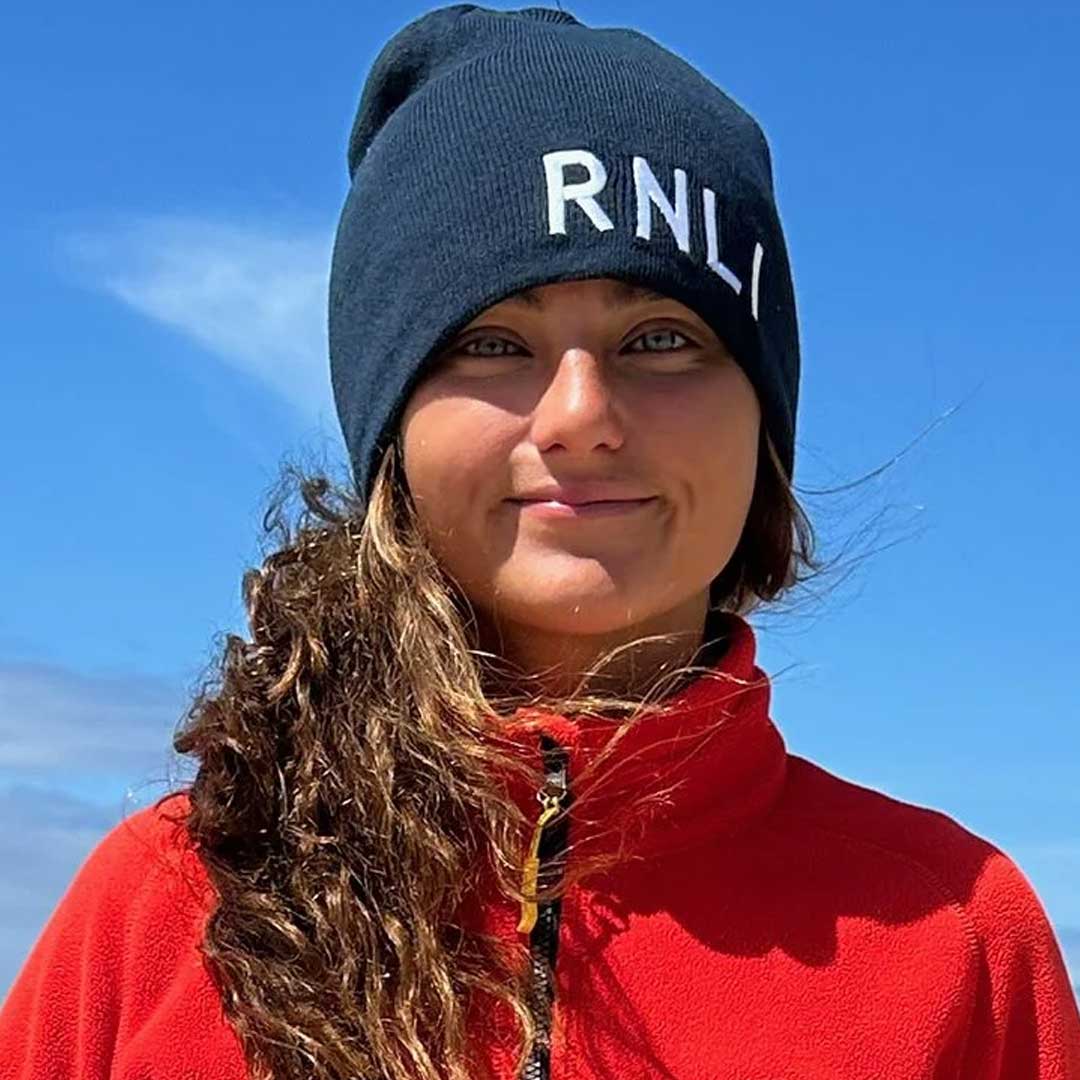 RNLI beach lifeguard Elise Irish wearing a blue RNLI hat and red lifeguard jacket