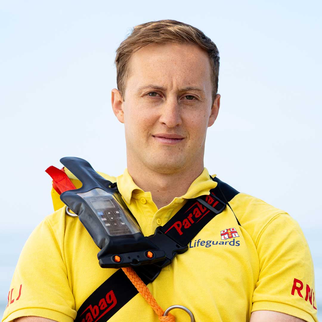 Lifeguard Matty McLeod wearing yellow lifeguard polo and a radio strapped to his chest poses for a photo