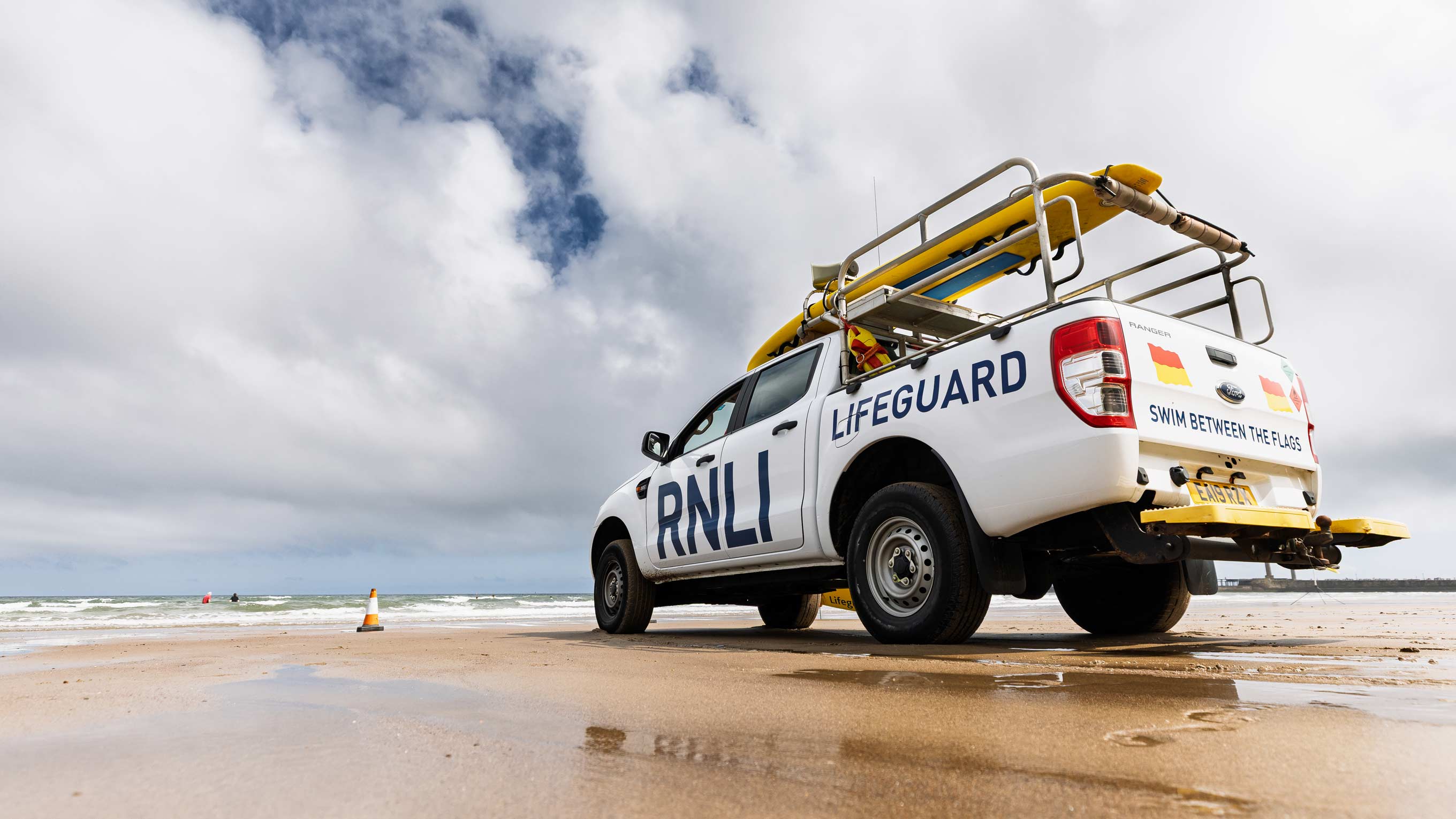 A white Ford Ranger lifeguard truck sits parked on a wet sandy beach facing the tide line