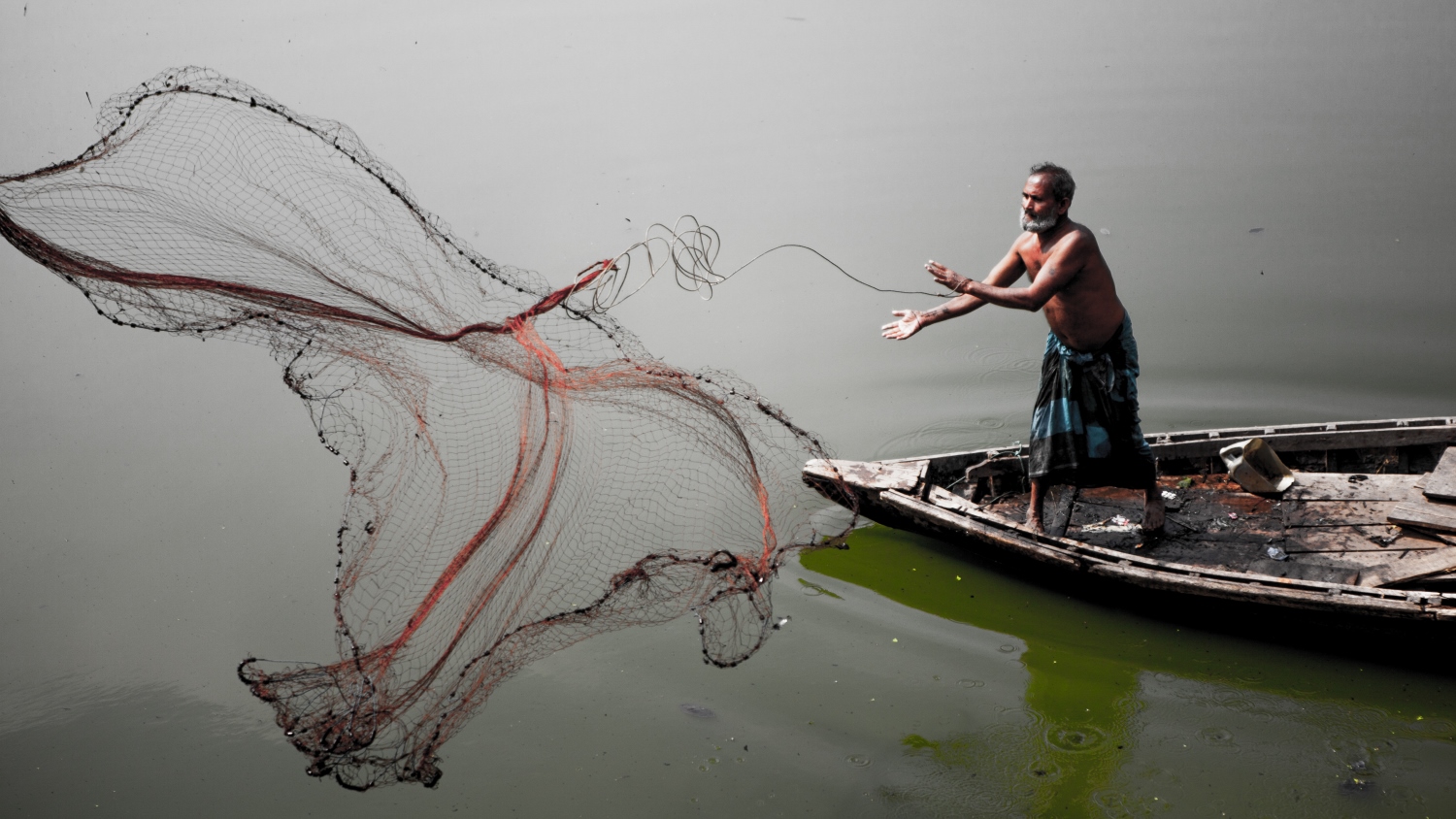 A fisherman casts his net on a river in Dhaka, Bangladesh