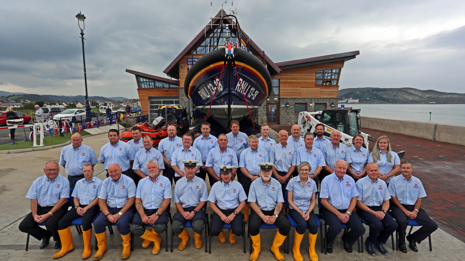 A group of volunteers are standing and sitting in front of the new Shannon class lifeboat and new Llandudno Lifeboat Station building